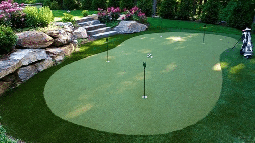 Landscaping services installing a putting green in a yard with retaining walls and gardens