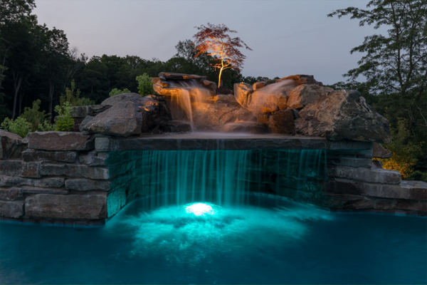 Captivating pool waterfall illuminated by custom lighting, creating a mesmerizing visual spectacle.