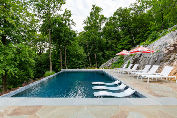 Enchanting backyard pool at night, enhanced by mesmerizing fire features, creating a warm and inviting ambiance.