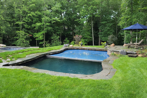 Tranquil pool nestled amidst lush nature, featuring an automatic pool cover for convenience and safety