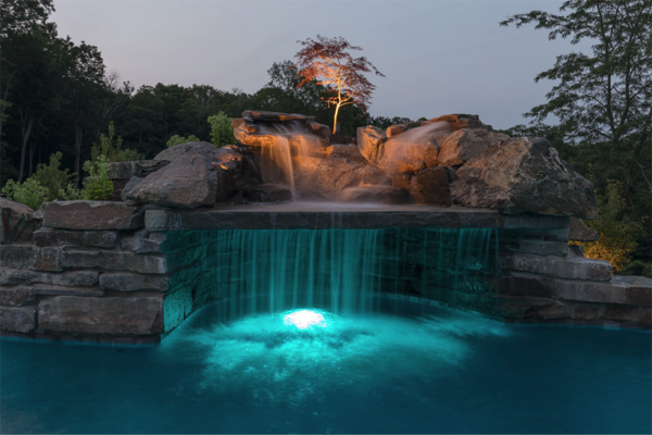 A breathtaking pool with an elegant rock grotto illuminated at night, showcasing stunning waterfalls and enchanting lighting features