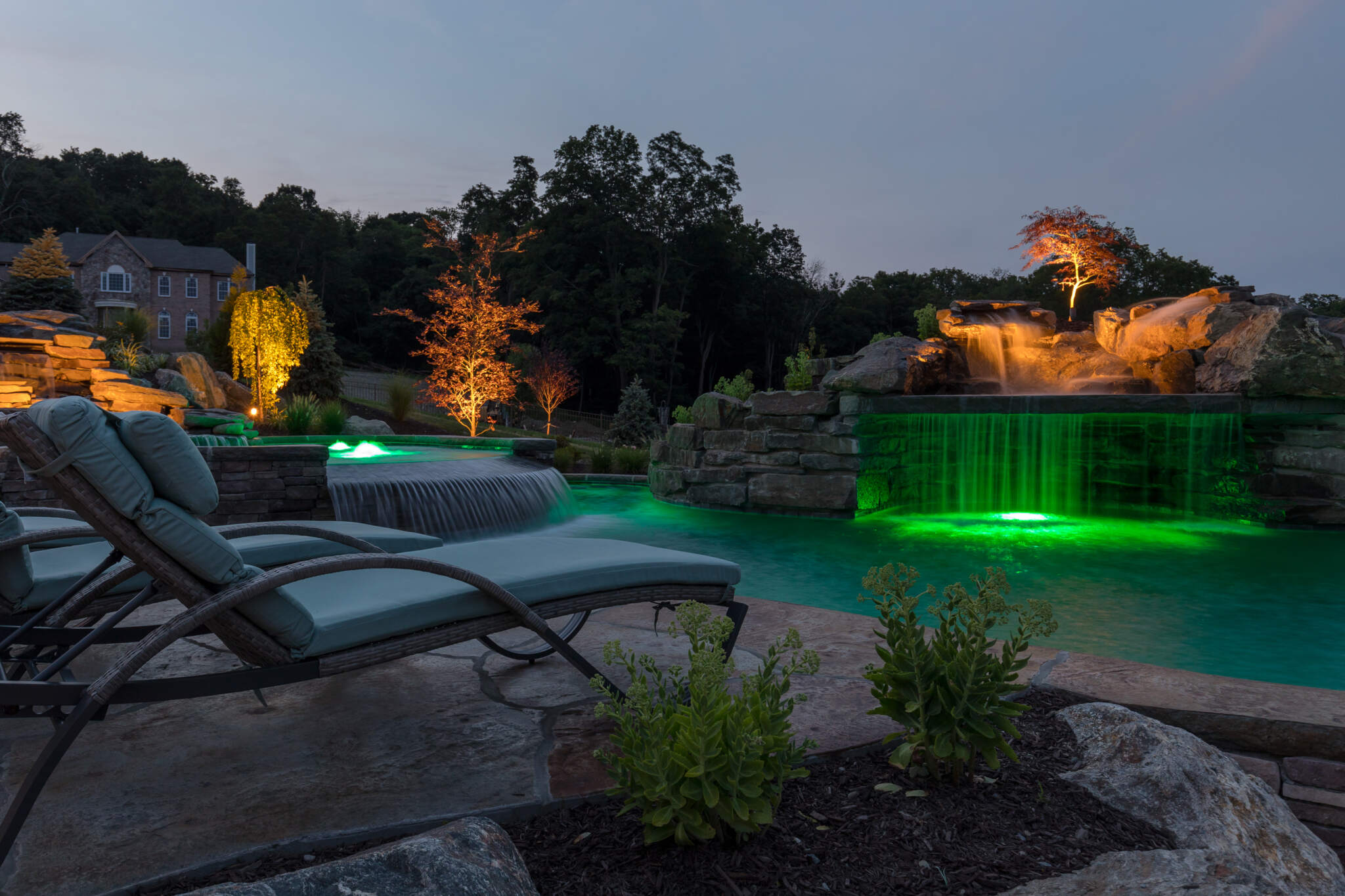 Natural stone encasing a hot tub and a sublime electrical instalaltion showing limelight with this inground pool design