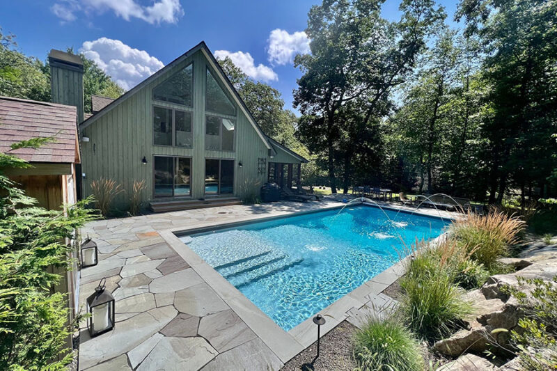 A backyard featuring a fiberglass inground pool surrounded by natural stone tiles, showcasing the benefits of fiberglass pools, including durability and aesthetics.