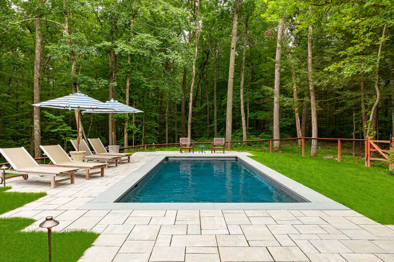 A serene outdoor setting featuring a fiberglass inground pool, surrounded by lush greenery and elegant stone tiles, ideal for relaxation