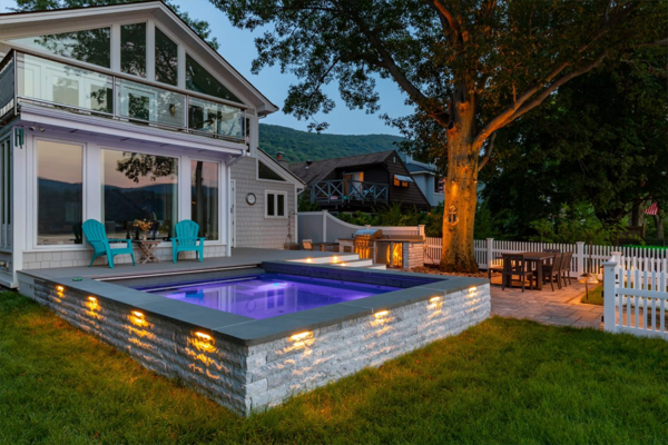 Elegant outdoor dip pool with ambient lighting, adjacent to a modern home and a cozy patio area under a large tree