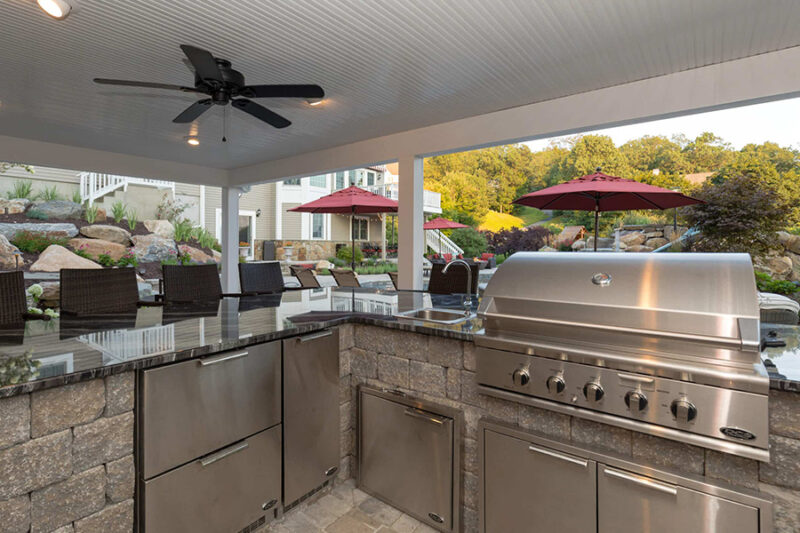 Luxury patio kitchen with stainless steel appliances, ample counter space, and seating area under a covered pergola