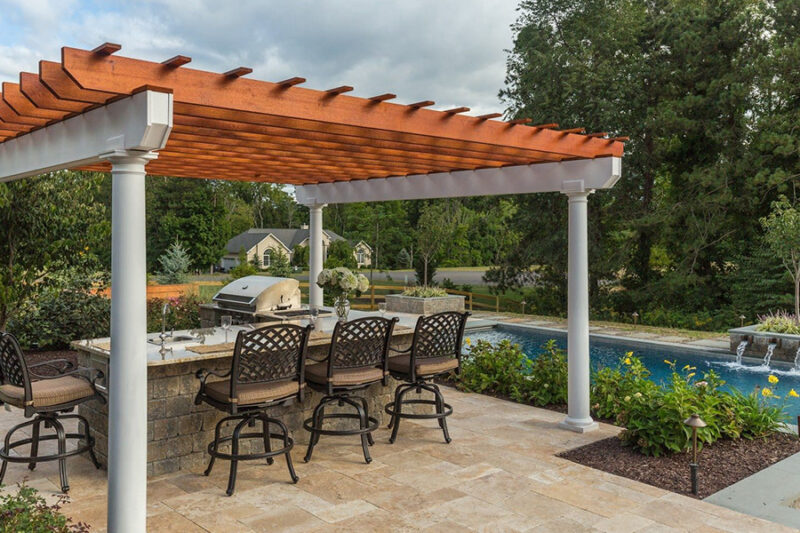 Outdoor kitchen ideas featuring a modern design with a pergola, bar seating, and a built-in grill beside a pool.