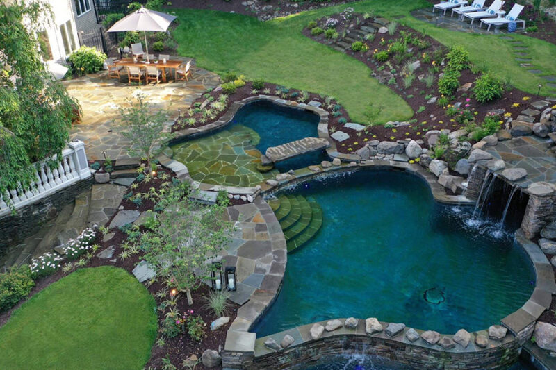 Aerial view of a backyard featuring a natural pool design with a waterfall and landscaped garden.