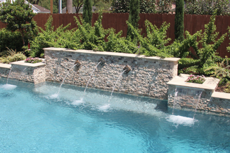 Elegant stone wall with sconces pouring water into a pool, showcasing unique water features in a lush garden setting