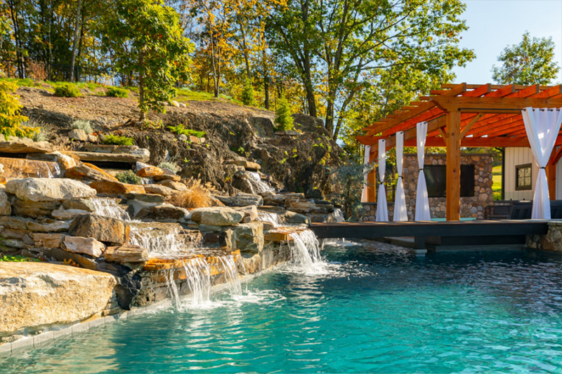 Luxurious backyard pool with cascading waterfalls and a pergola, showcasing elegant pool water features.