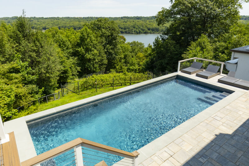 Rectangular pool by a modern home overlooking a lush green forest and lake, showcasing elegant pool shapes