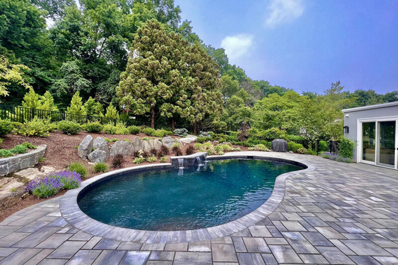 Serene backyard with a kidney pool shape, complete with a waterfall and lush landscaping