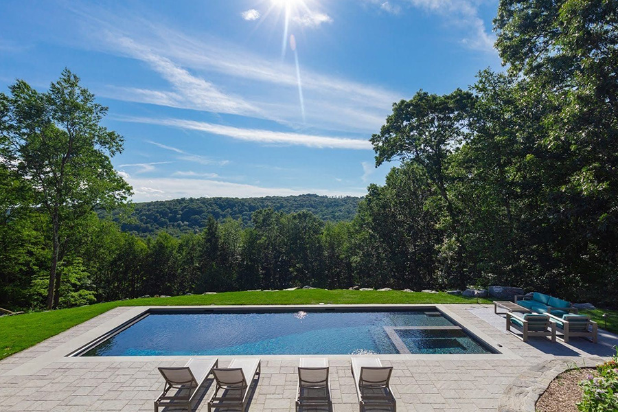 A fiberglass spool in a serene backyard setting with lounge chairs, surrounded by lush greenery and a scenic forest view