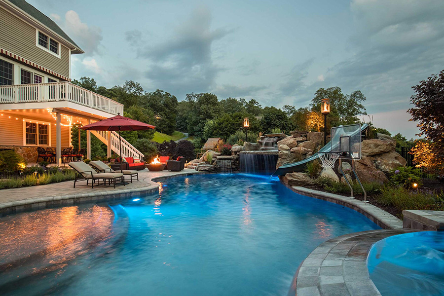 Luxurious backyard pool featuring a slide, waterfall, fire pit, and ambient lighting, one of the top fiberglass spools for relaxation