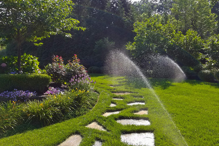 Manicured lawn with sprinklers, flower beds, and a stone pathway, illustrating landscaping tips for a tranquil outdoor space