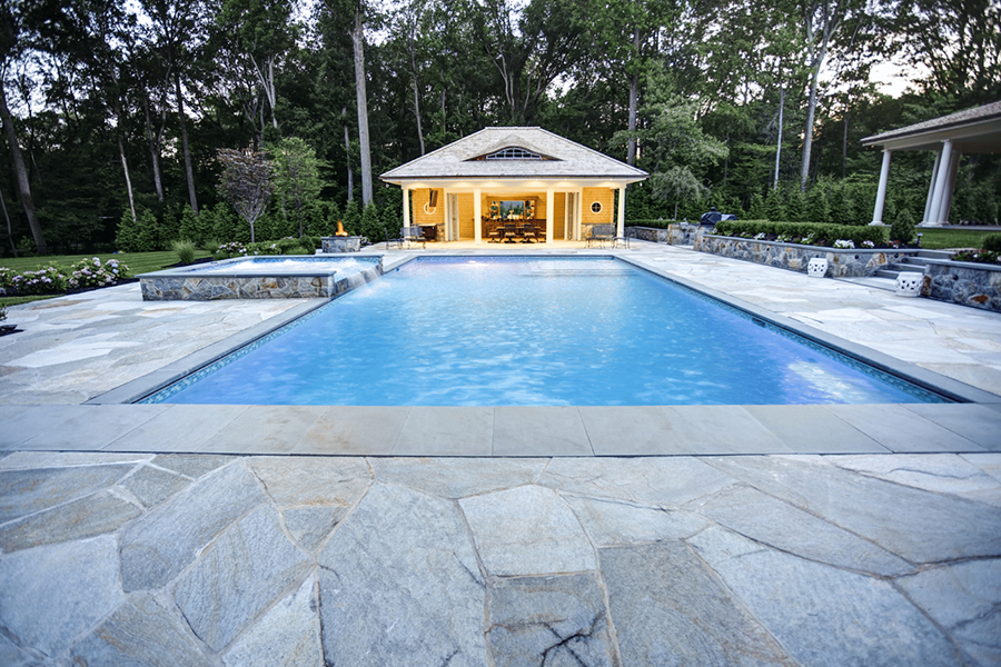 Modern rectangular pool with stone decking and greenery, showcasing elegance and functionality that is part of modern rectangle pool designs